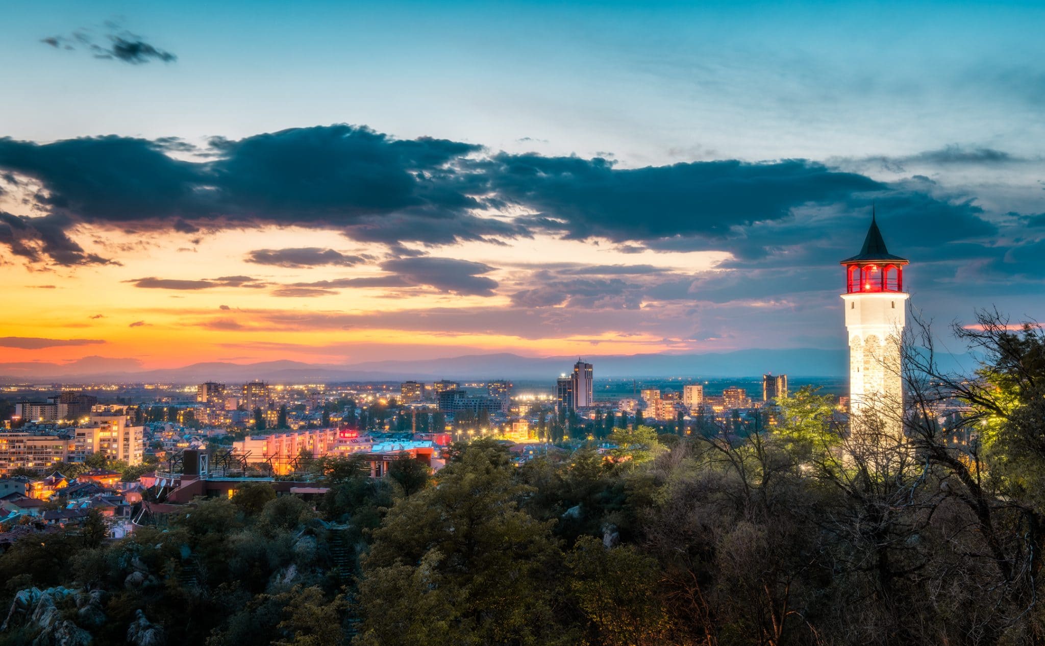 Vedere la apus de soare a Turnului cu Ceas din Plovdiv care strălucește, stând înalt deasupra liniei de orizont a orașului cu culorile orei de aur pe cer.