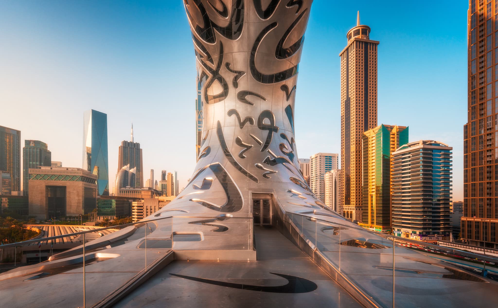 O terraço de observação do Museu do Futuro, no Dubai, com a sua fachada caligráfica em aço inoxidável a erguer-se sobre o horizonte do Dubai ao amanhecer.